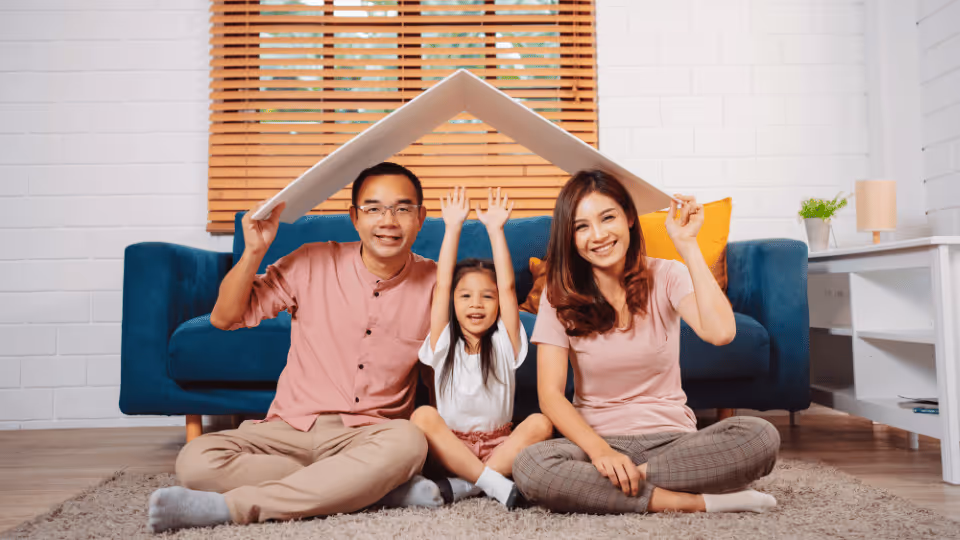 A family sits on the floor, resting their heads on a house model, symbolizing the importance of insurance coverage