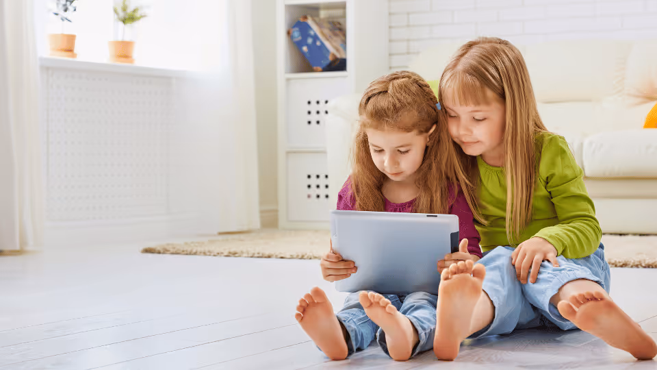 Two young girls seated on the floor, engaged with a tablet, exploring options for finding a provider nearby.