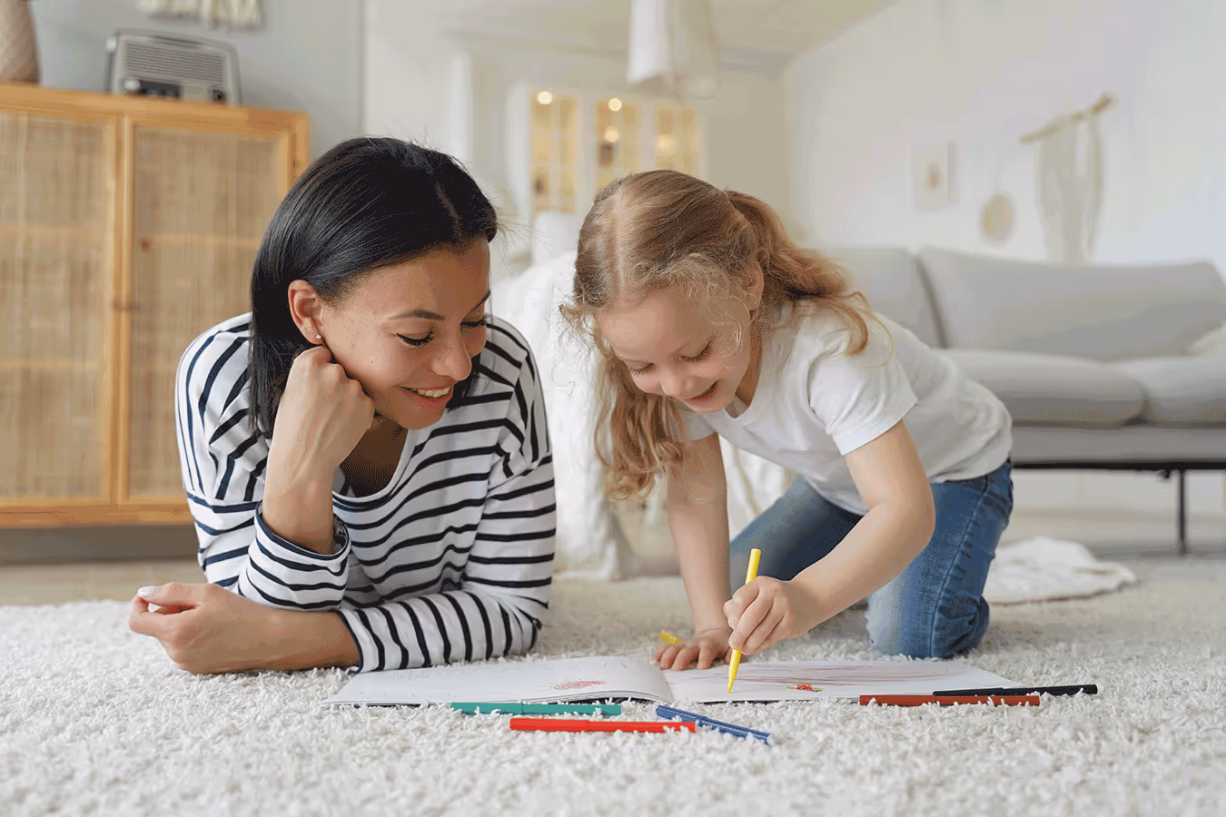 A woman and child lay on the floor, drawing together to enhance fine motor skills through coloring.