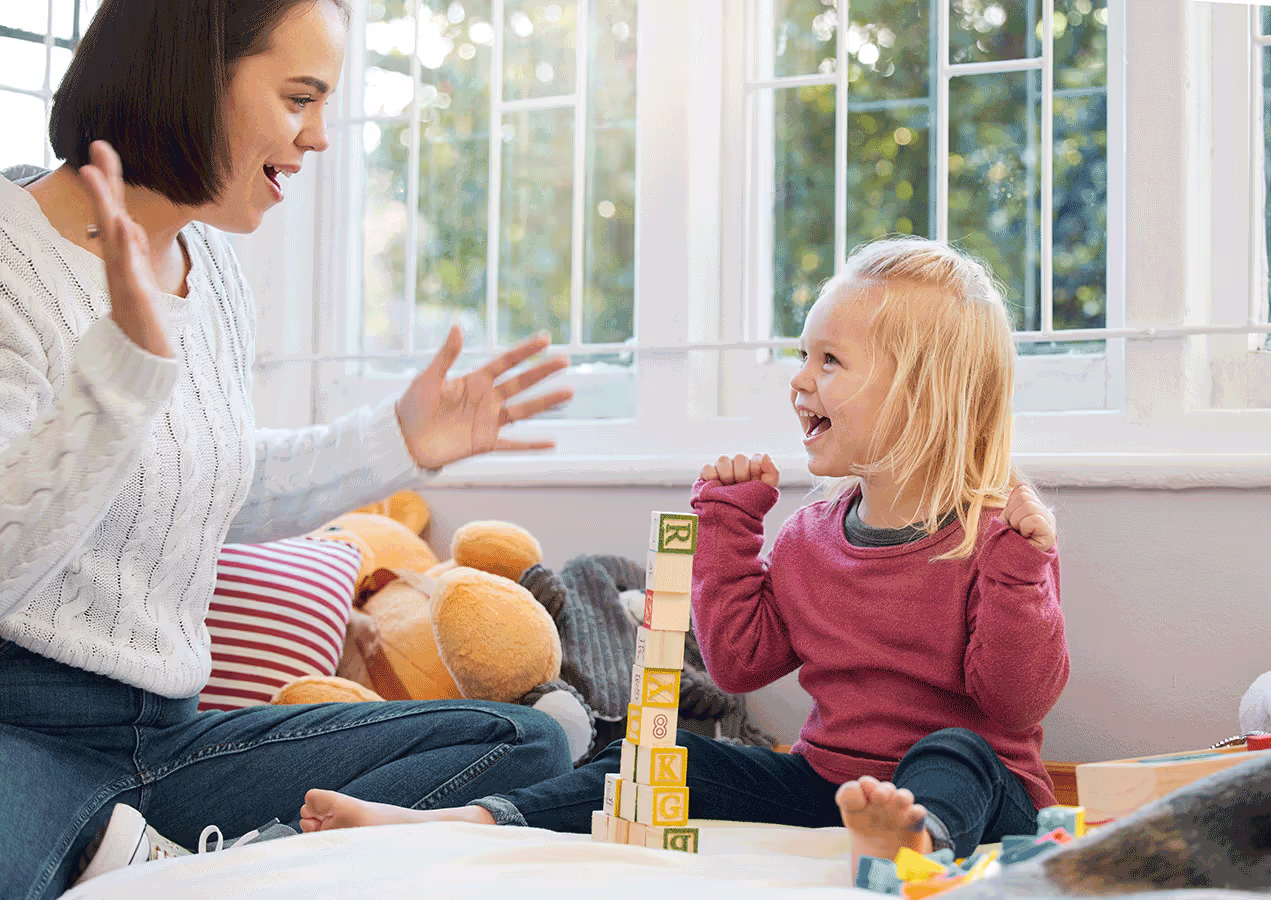 A female therapist and a child happily playing with colorful blocks on the floor, building structures together.