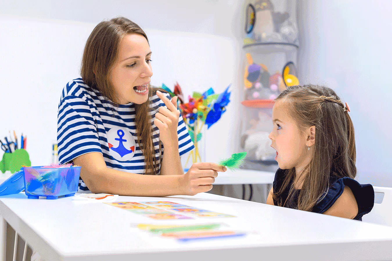 A woman and a young girl sit at a table, engaged in a speech therapy activity focused on articulation skills. 