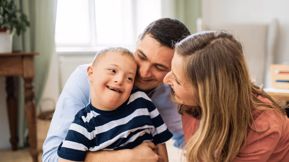 A man and woman embrace a child, symbolizing support and love, representing developmental disability councils in Austin.