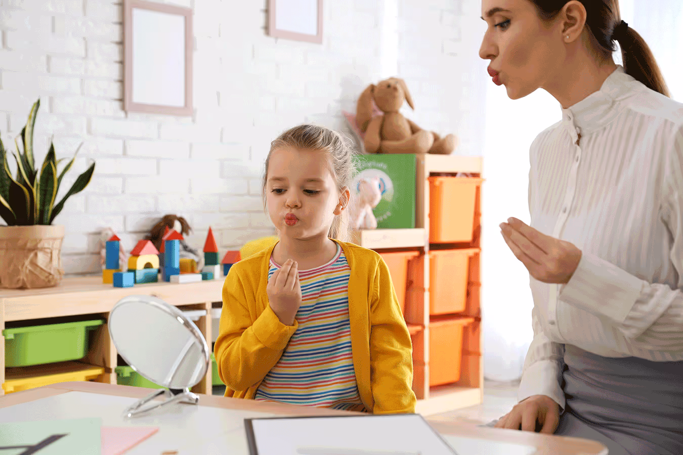 A therapist helps a girl in a playroom setting, assisting her with speech therapy and sound articulation.