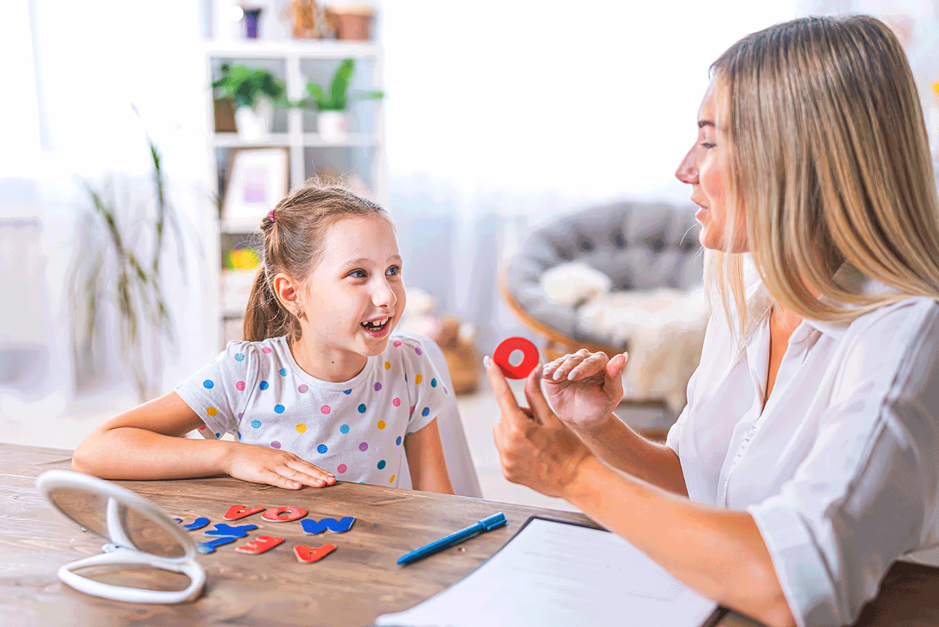 A therapist and a child sit at a table, focused on a word game while practicing speech sounds during their therapy session.