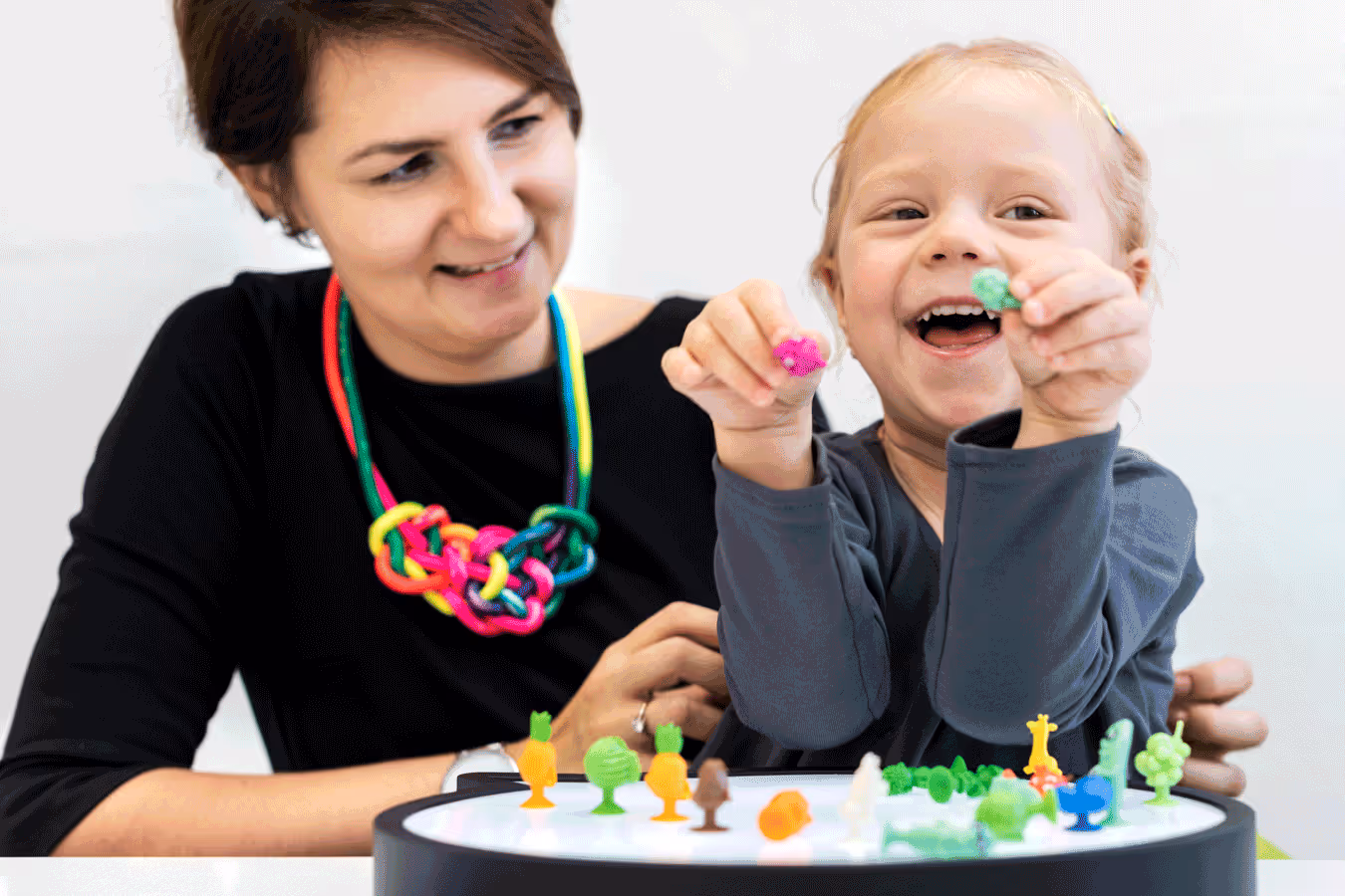 A woman and a child engage with vibrant toys, enjoying a playful moment in pediatric therapy.