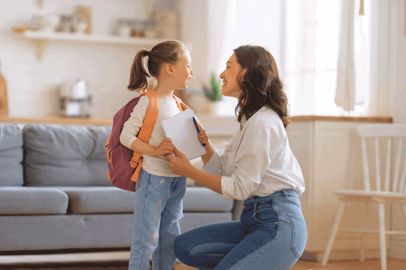A woman and a child wearing a backpack are in the living room, both excited and ready for the school day.
