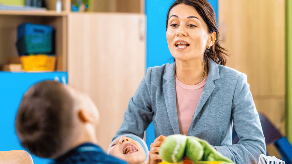 In a classroom, a woman engages with a child, representing speech therapy services offered by Boston speech pathologists