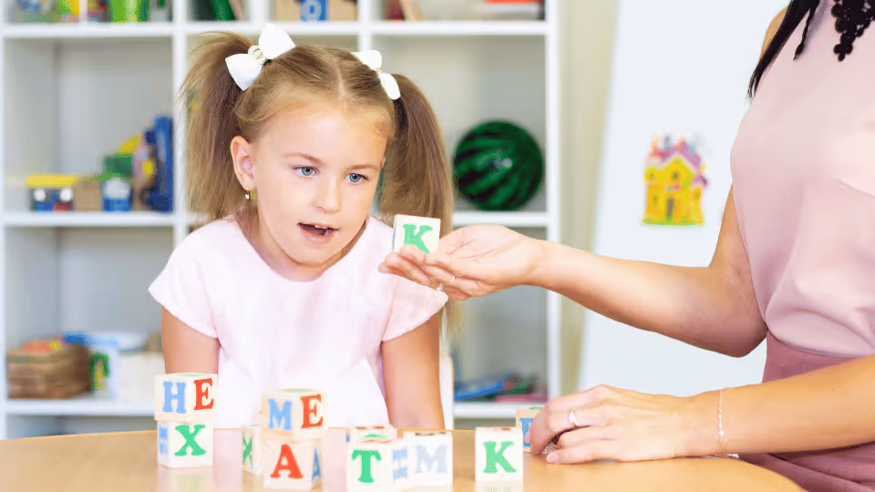 A woman teaches a young girl to spell letters, highlighting early intervention in pediatric speech therapy