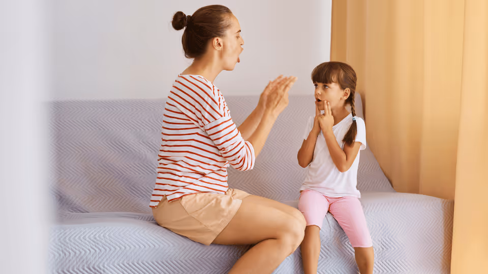 A woman and a young girl sit together on a couch, engaged in early intervention and pediatric speech therapy activities