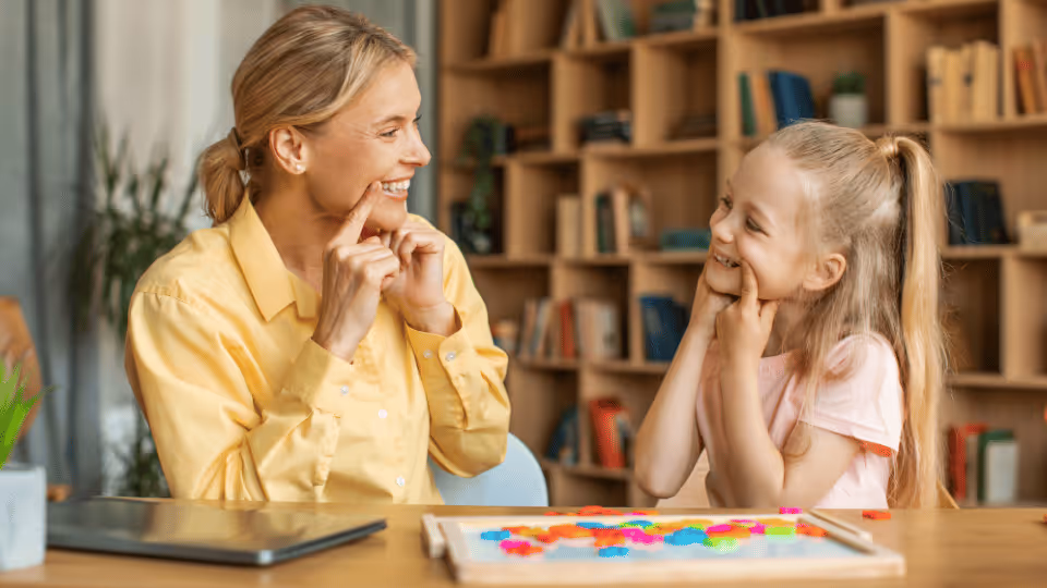 A woman and a young girl sit at a table with a laptop, discussing pediatric speech pathology opportunities in Austin, Texas