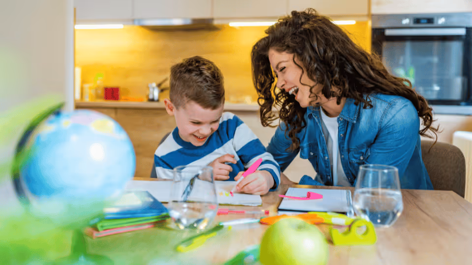 A woman and a child are seated at a table, using a pencil and paper, illustrating a pediatric speech pathology session