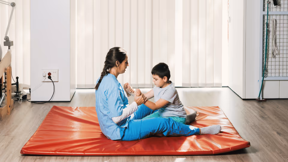 A woman and child sit on a red mat, highlighting pediatric physical therapy opportunities in Boston, Massachusetts.
