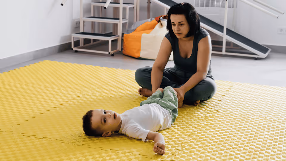 A woman and a child interact on a bright yellow floor, highlighting pediatric physical therapy opportunities in Boston