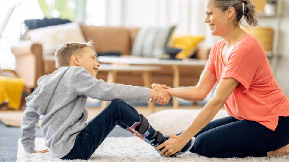 A woman and a boy sit on the floor, shaking hands, symbolizing pediatric physical therapy opportunities in Houston, Texas.