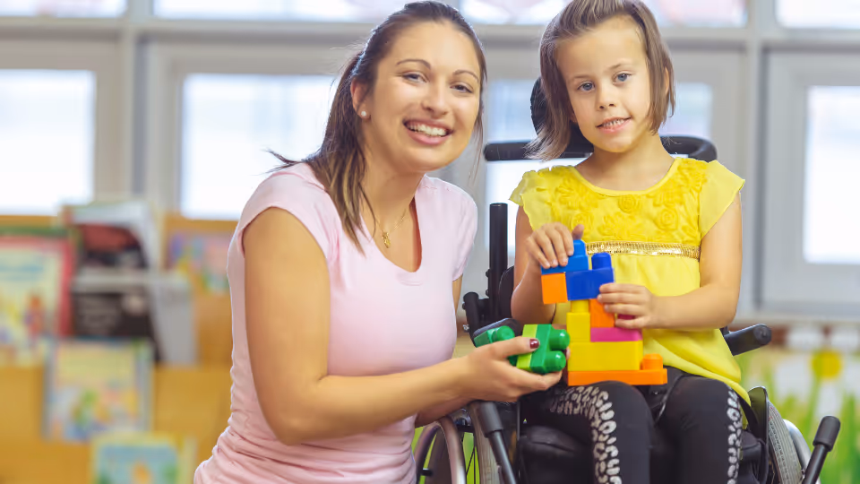 A woman in a wheelchair smiles as a child builds with blocks, representing parent advocacy programs in Boston