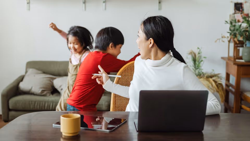 A woman and two children are seated at a table with a laptop, involved in a parent support group meeting in Boston