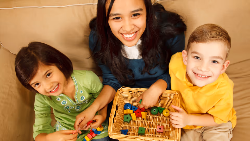A woman and two children sit on a couch, playing with a basket of wooden blocks, highlighting family resources in Austin, TX