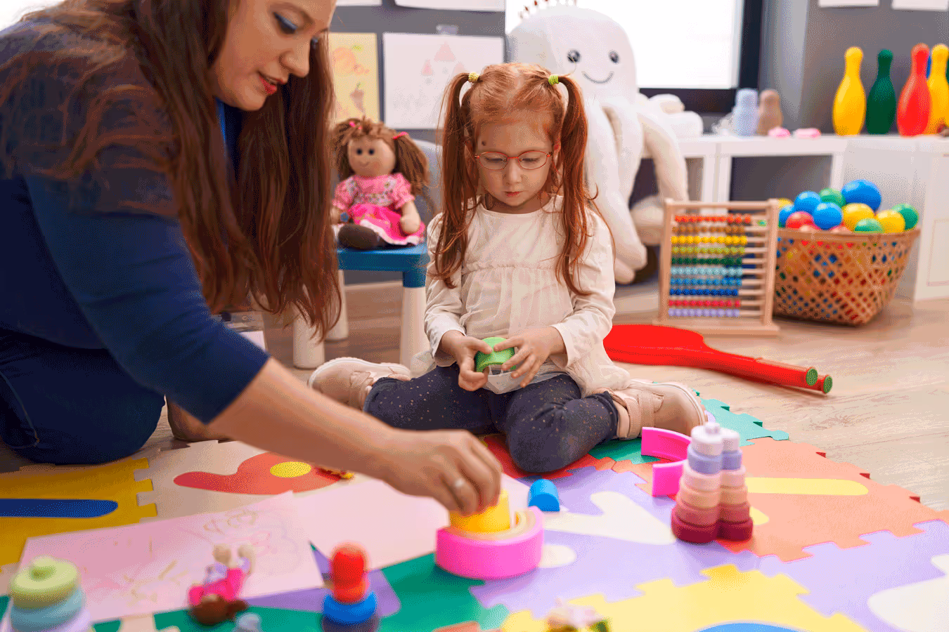 A woman and child engaged in play with vibrant toys in a colorful playroom setting.