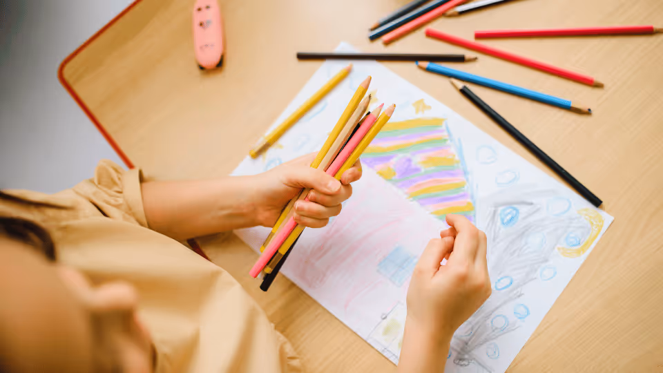 A child focused on drawing with colored pencils on paper, illustrating summer's role in enhancing motor skills