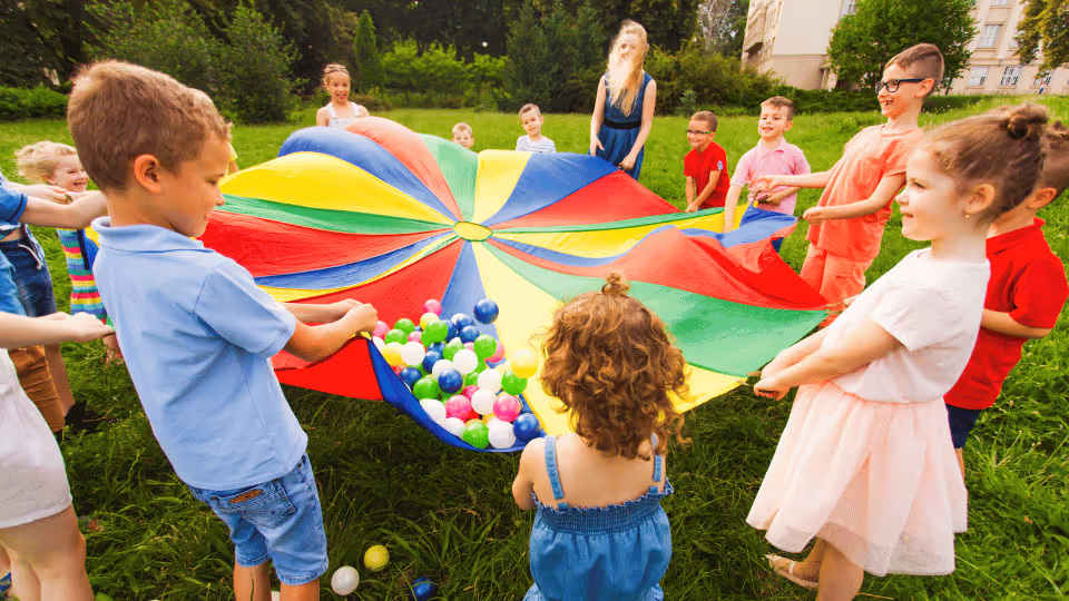 Children joyfully playing with a colorful umbrella on green grass, enjoying creative sensory-friendly summer fun.