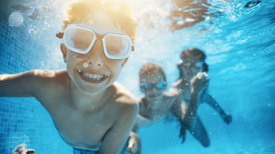 A group of children joyfully swimming together in a pool, highlighting the benefits of water play in pediatric physical therapy.
