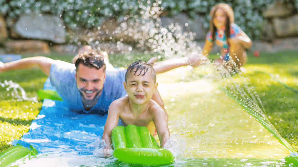 A man and a child enjoying a fun moment on a water slide, illustrating common aquatic therapy activities.