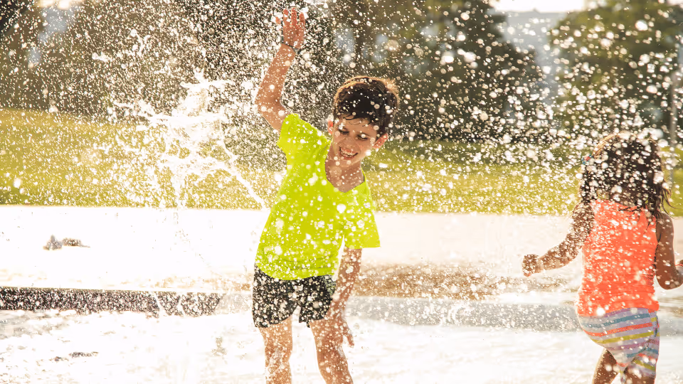 Two children joyfully playing in a water fountain, enjoying summer therapy through engaging water play activities.
