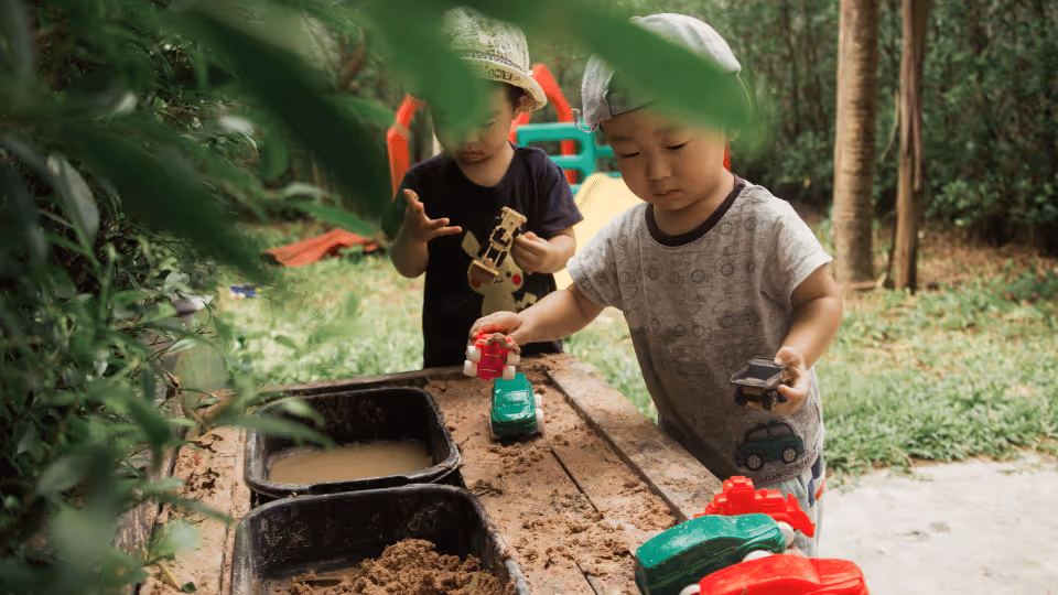 Two kids in rain boots pick herbs outside, participating in sensory play to enhance occupational therapy skills.