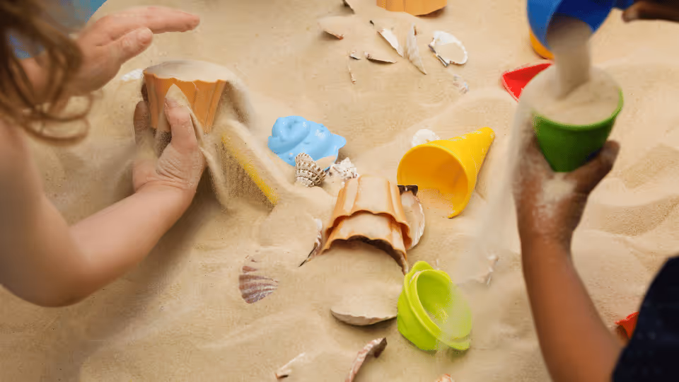 Children joyfully playing in sand with colorful toys, engaging in sensory play that supports childhood development.