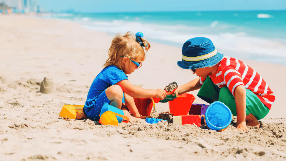 Two children joyfully playing with sand at the beach, exploring textures and sounds in a natural sensory playground.