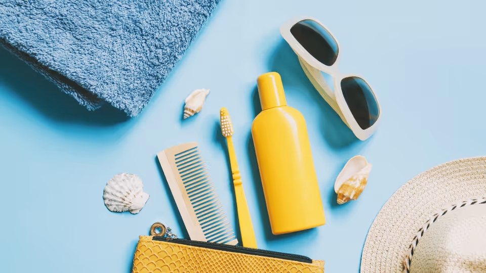 A beach hat, sunglasses, towel, and comb arranged on a blue surface, illustrating essential items for a family beach trip.