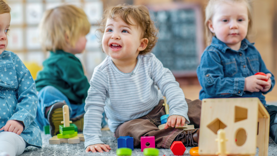 Three children constructing with wooden blocks on a classroom floor, focused on their creative play.