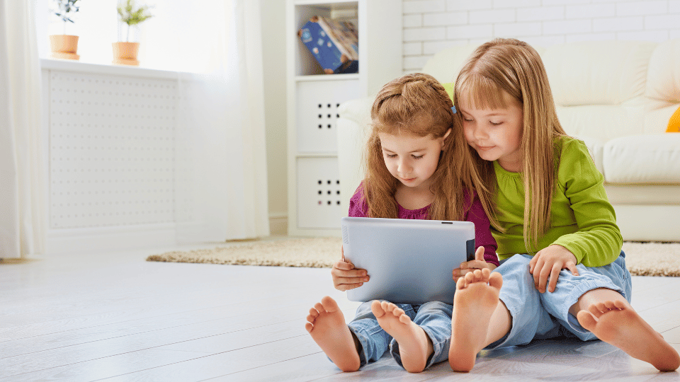 Two young girls seated on the floor, engaged with a tablet, exploring options for finding a provider nearby.