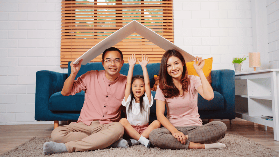 A family sits on the floor, resting their heads on a house model, symbolizing the importance of insurance coverage