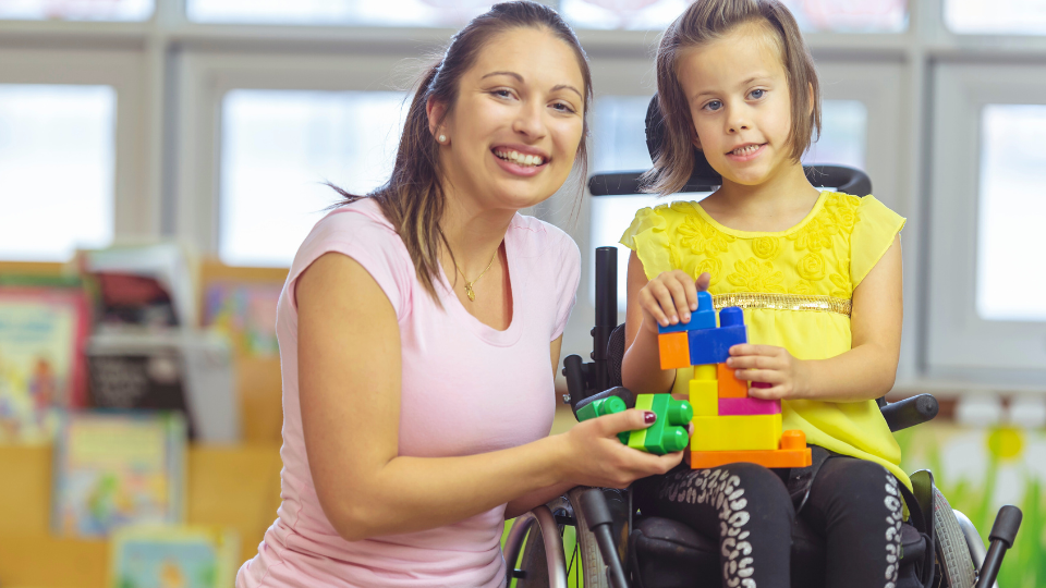A woman in a wheelchair smiles as a child builds with blocks, representing parent advocacy programs in Boston