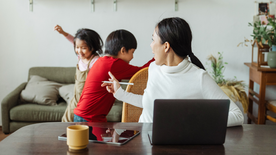 A woman and two children are seated at a table with a laptop, involved in a parent support group meeting in Boston
