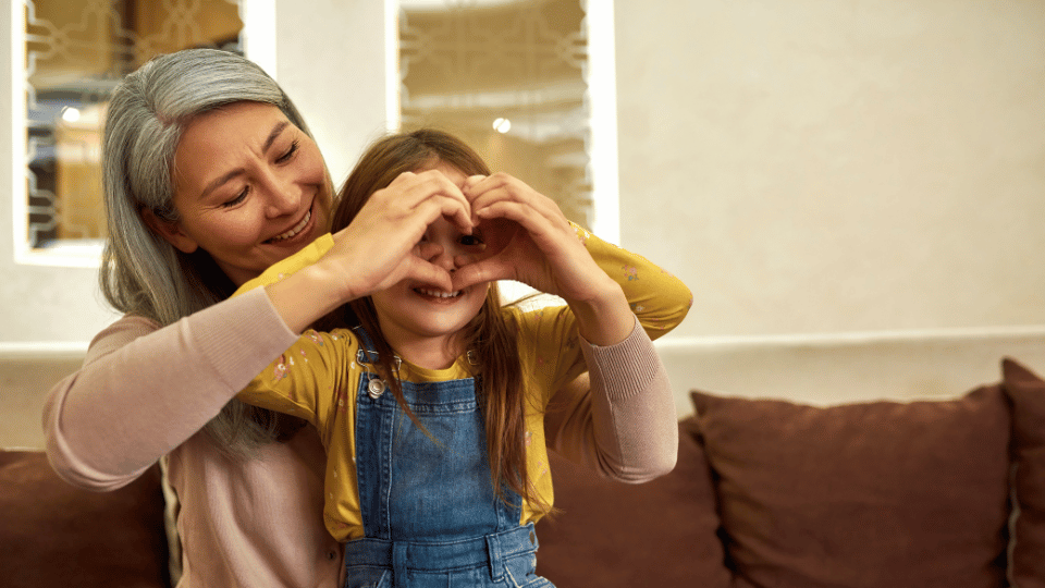 A woman and a young girl form a heart shape with their hands, symbolizing love and connection in a parent support group.