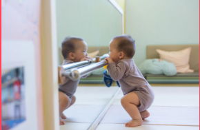 Baby on their stomach on a play mat lifting their head to look at a shatterproof floor mirror