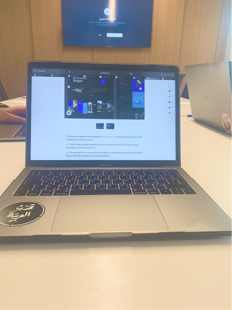 Open MacBook Pro on table showing a web design project page with two other laptops in background.