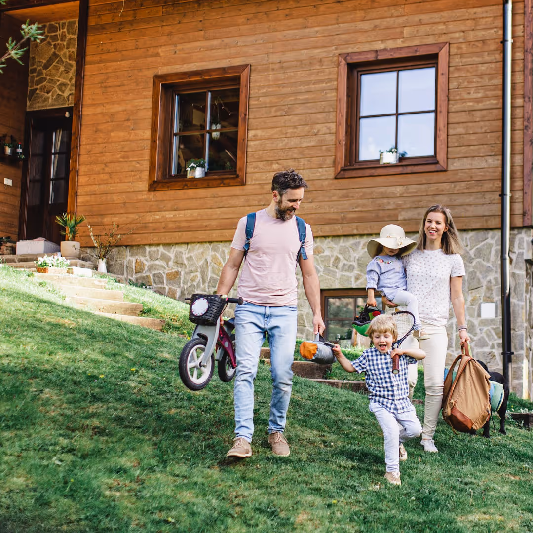 Familie mit zwei Kindern verlässt ein gemütliches Holzhaus im Grünen für einen Ausflug