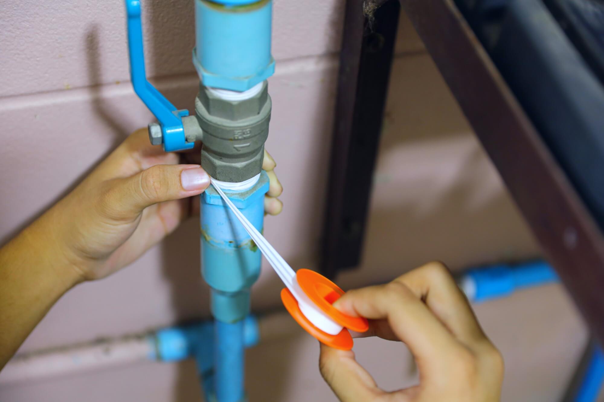 Plumber applying Teflon tape to blue water pipes for leak prevention and secure connection.