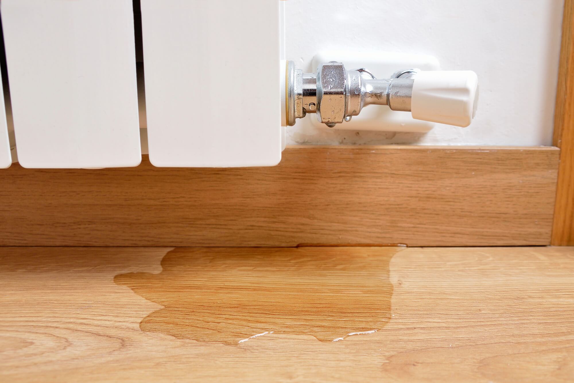 Leaking radiator valve causing water puddle on wooden floor.