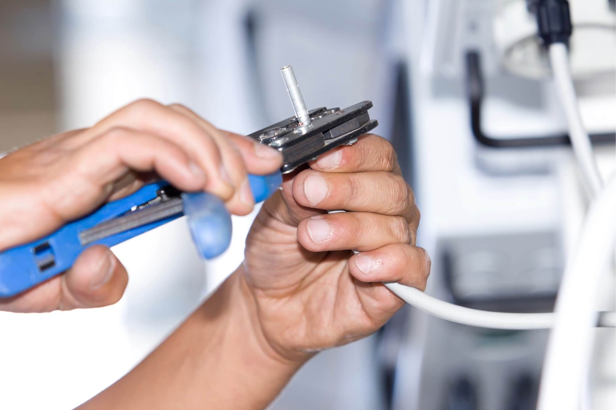 Hands using a crimping tool to connect a cable in an electrical installation.