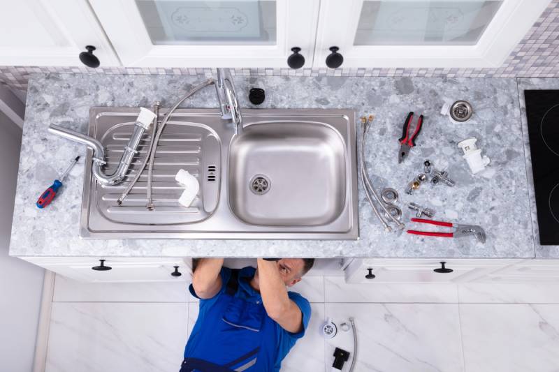 Plumber under sink repairing pipes.