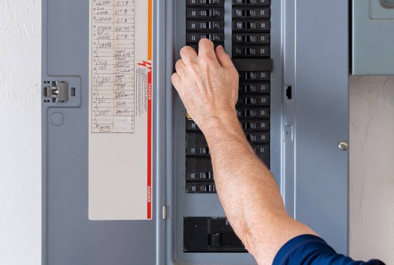 Hand adjusting circuit breaker in electrical panel.