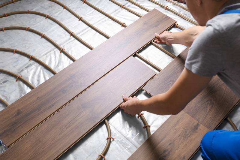 Person installing wood flooring over radiant heating system.