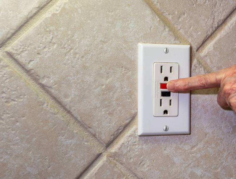 Finger pressing GFCI outlet reset button