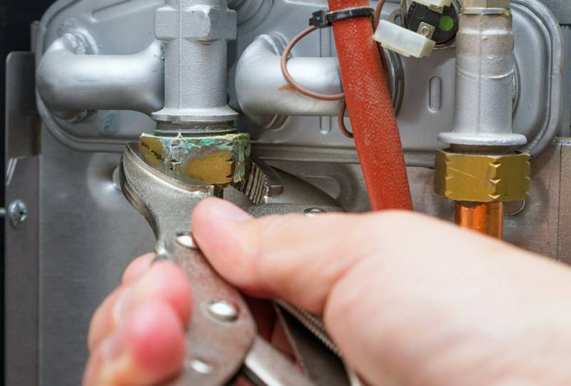 Hand using pliers on heater pipes