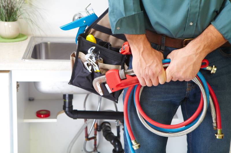 Plumber holding tools and hoses near a sink.