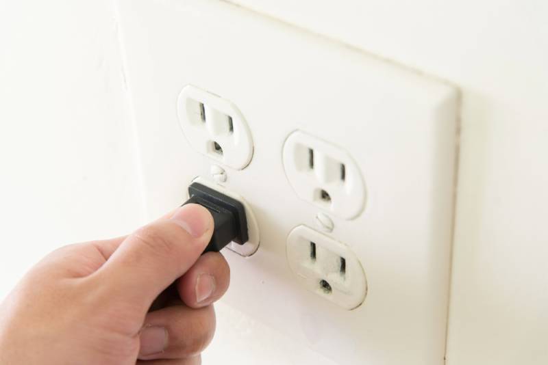Hand plugging device into dual electrical outlet.